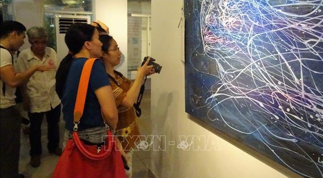 Посетители рассматривают картины на выставке. Фото: VNA